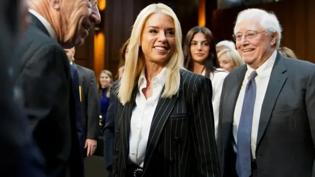 Pam Bondi, wearing a black pin striped suit, smiles in the hearing room