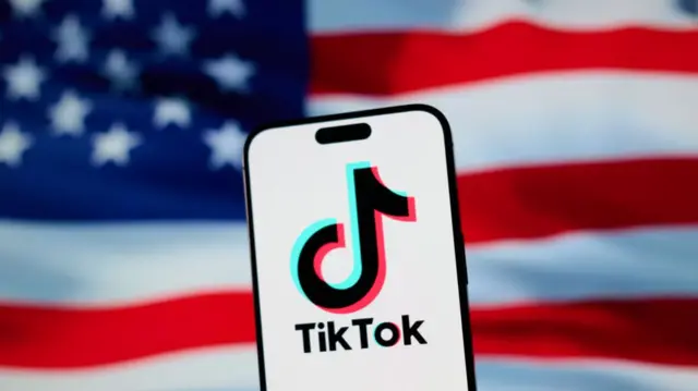 Телефон із логотипом TikTok на передньому плані та трохи не в фокусі американським прапором на задньому плані