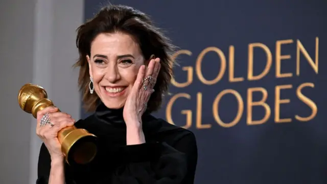 Fernanda Torres holding her Golden Globe statue and smiling