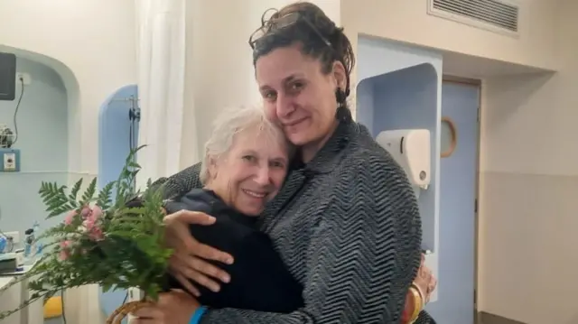 Efrat Moses hugs her aunt, Margalit Moses, in a room with light blue and cream walls