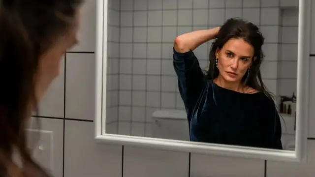 Demi Moore in The Substance, looking at her face in the mirror.