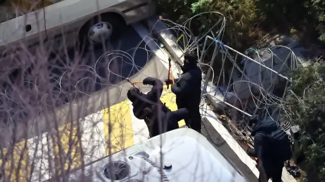 Two people cutting through barbed wire with wire cutters