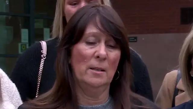 Angela Dawes with long dark hair and a grey jumper and black coat speaking outside Preston Crown Court