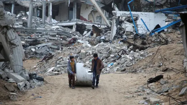 Palestinian boys drag an object past the rubble of houses destroyed in previous Israeli strikes, ahead of a ceasefire set to take effect on Sunday, in Khan Younis in the southern Gaza Strip January 16