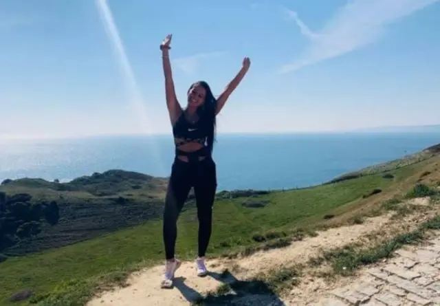 Kiena Dawes standing near water on a hilly bank with arms in air