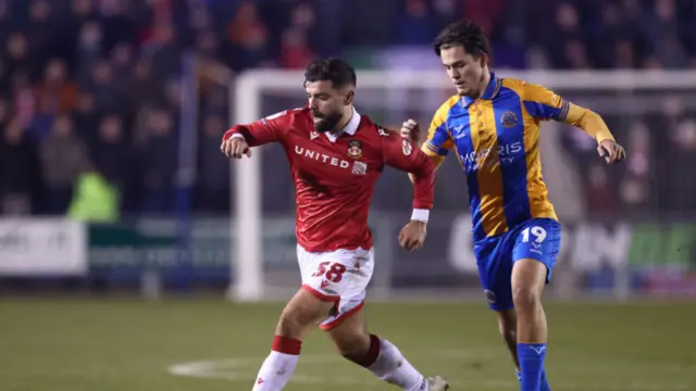 Elliot Lee of Wrexham runs with the ball whilst under pressure from Leo Castledine of Shrewsbury Town