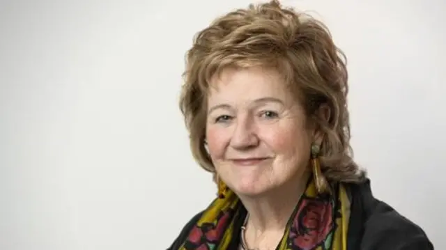 Prof Alexis Jay smiles in front of a grey background wearing a scarf