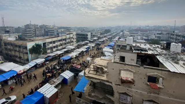 A long stretch of a street market with surrounding damaged buildings and a grey sky above