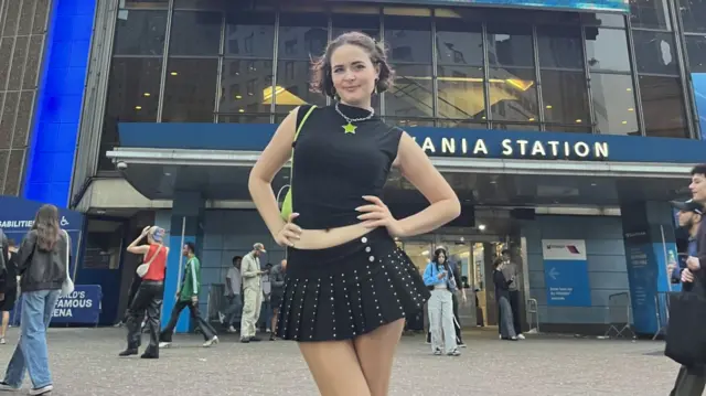 TikTok creator Kelley Heyer stands in front of a stadium with a Charlie XCX billboard behind her.