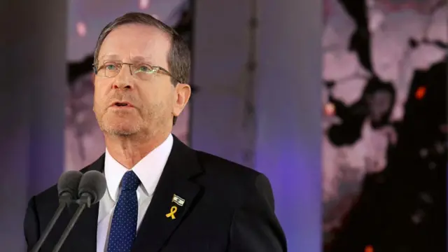 Israel's President Isaac Herzog delivers a speech during a memorial ceremony. He wears a pin with the Israeli flag and a yellow tie, to commemorate the hostages still being held in Gaza