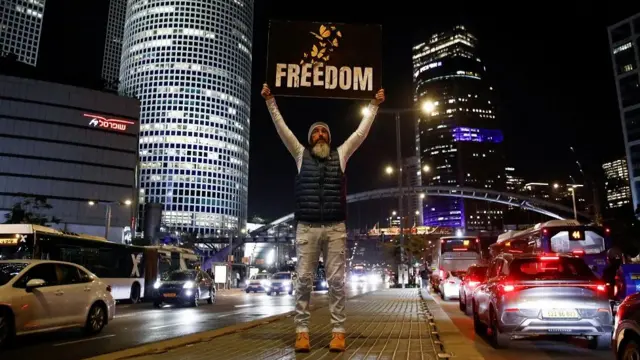 A man holds a placard on a road reading 'Freedom' as cars go by