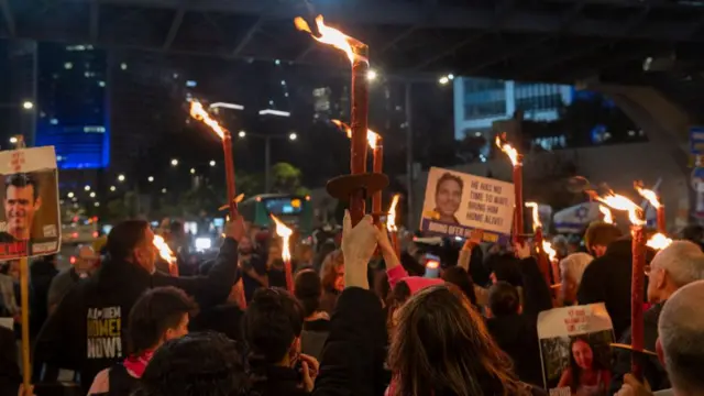 A crowd of people holding placards of people's faces. Many in the crowd are holding lit red candles above their heads.