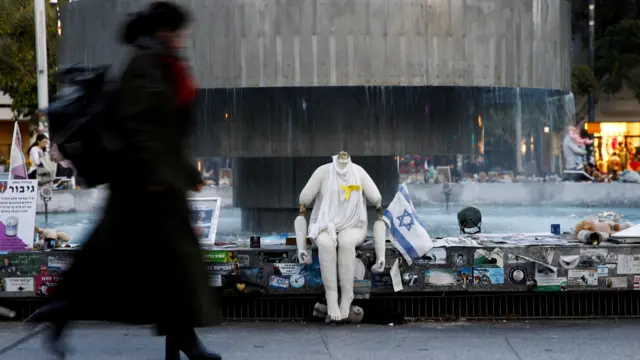 woman walks near pictures and memorabilia related to fallen soldiers, hostages and people killed during the 7 October 7 attack by Hamas,