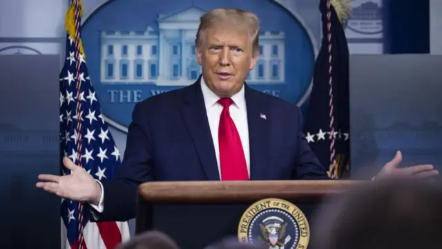 An image of President Donald Trump standing in front of a podium in the White House, he is wearing a blue suit with red tie