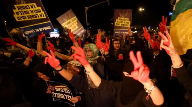 Protestors holding up placards in Hebrew and making the V sign with their hands