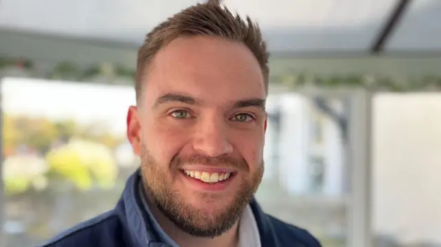 A man with short brown hair and a beard is smiling at the camera