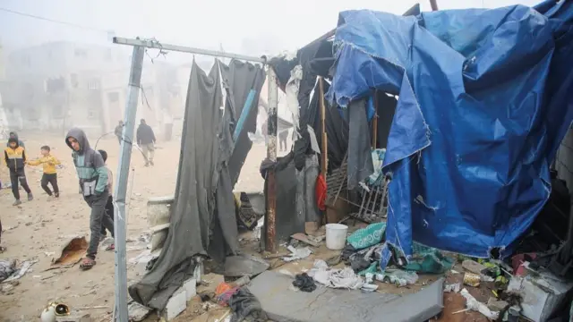 Palestinian boys stand near a damaged tent for displaced people, after an Israeli air strike