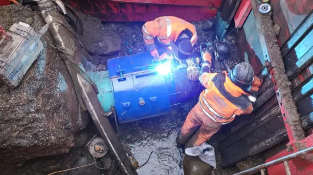 Engineers in orange suits are seen fixing a pipe