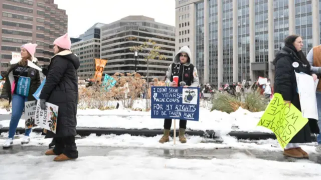 A person stands in the snow with a sign that says: I didn't serve 8 years marine corps for my rights to be taken away