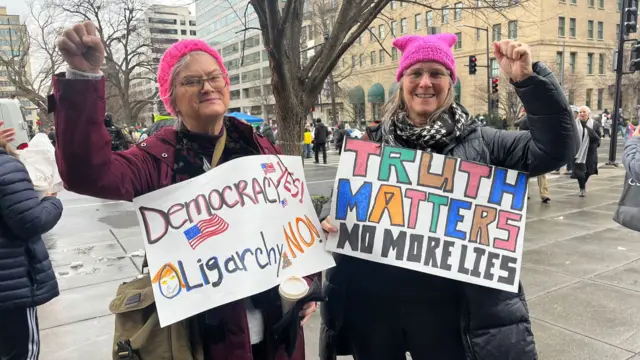 People hold up signs that say Democracy Yes, Oligarchy No. And one sign that reads: Truth Matters no more lies.