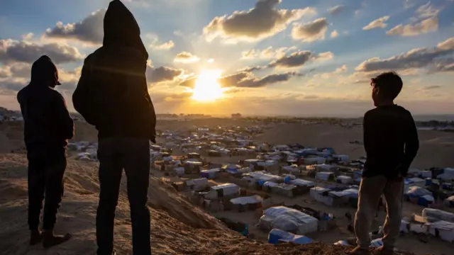 Palestinians watch the sunset next to a camp for internally displaced people in the southern Gaza Strip, on the eve a ceasefire between Israel and Hamas was set to take effect