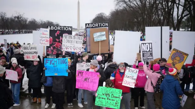 A crowd holding placards stands at the foot of the Washington Monument