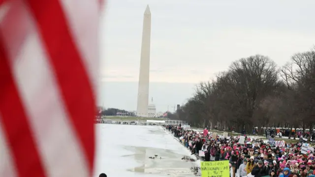 A crowd holding placards marches past the Washington Monument