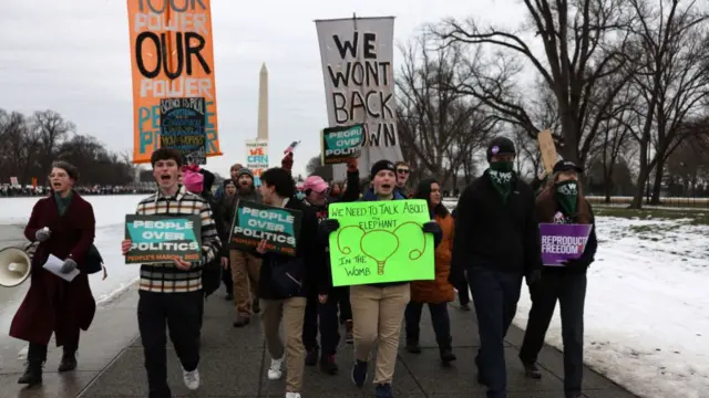 People march in front of the Washington Monument in DC holding placards that read various messages to express their displeasure with Donald Trump.