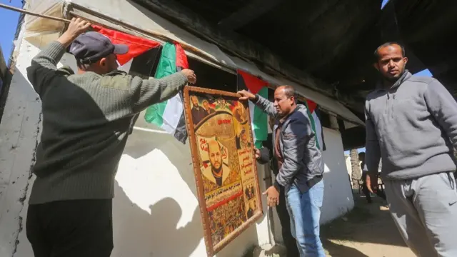 Three men hang up Palestinian flags and a board showing a man's face on a white wall