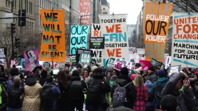 A large group of people hold signs with various statements on them, including will not be silent, our power, people power and unite for change.