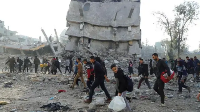 Internally displaced Palestinians make their way past rubble