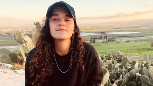 Emily Damari, an Israeli hostage, sits with a cap on in front of cacti