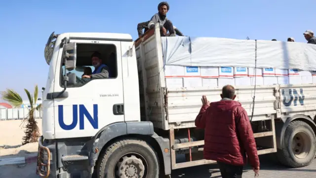 A UN aid truck in Gaza in December 2024. A man sits on top of boxes loaded on the back and a man on the street waves