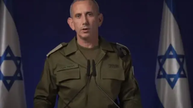 IDF spokesman Daniel Hagari, wearing green combat, speaks to reporters in front of two Israel flags