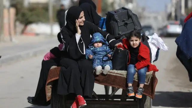 A woman sitting next to a baby and little girl on the back of a donkey cart