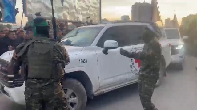 Hamas gunman stand guard outside of the Red Cross vehicles that are holding the three Israeli hostages.