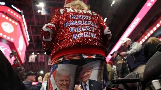 A woman wearing a red and sparkly "Make America Great Again" jacket, and trousers with Trump's face on them