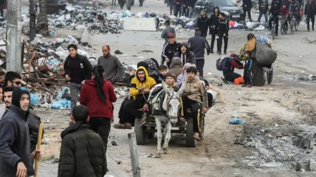 Street scene in Gaza city, with a group of people travelling on a donkey cart and others walking along the street which is dotted with piles of rubbish