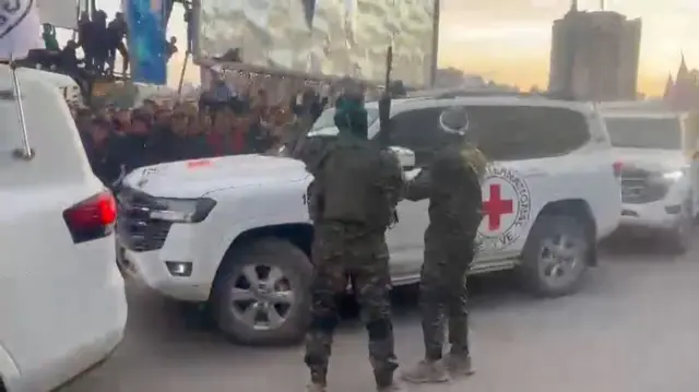 Hamas fighters escort Red Cross white vans carrying hostages through the crowd in Gaza