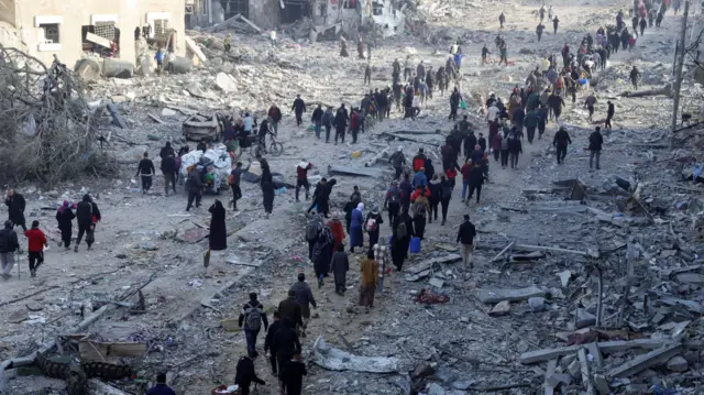 Palestinians walk in lines among rubble in Gaza