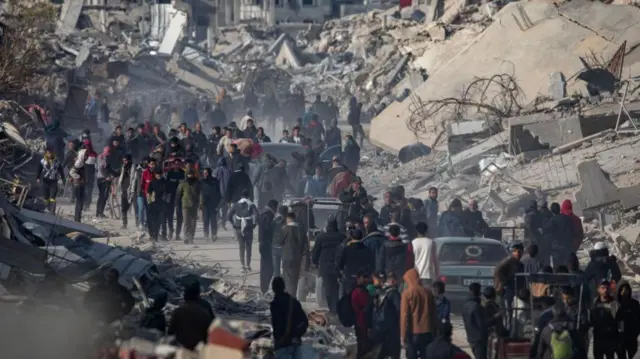 Internally displaced Palestinians make their way past rubble