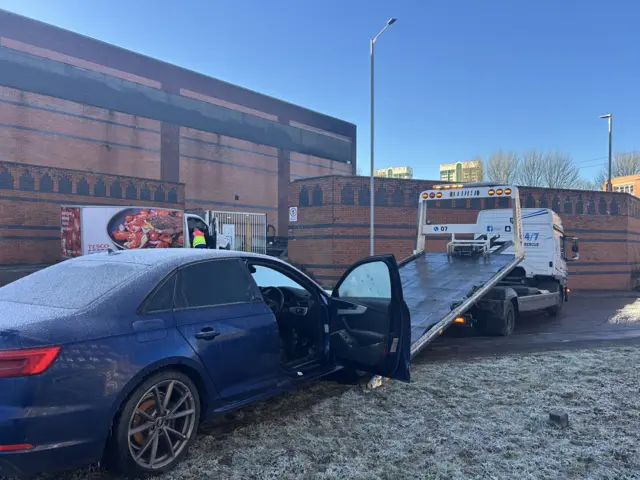 A blue Audi being placed onto a recovery vehicle