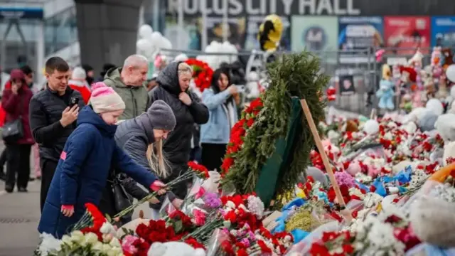 People lay flowers at a memorial for the Moscow attack in March. People are wearing winter gear and there are flowers.