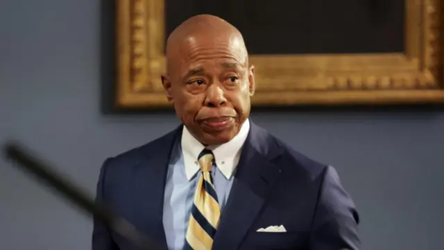 Mayor Eric Adams wears a blue suit and yellow tie.