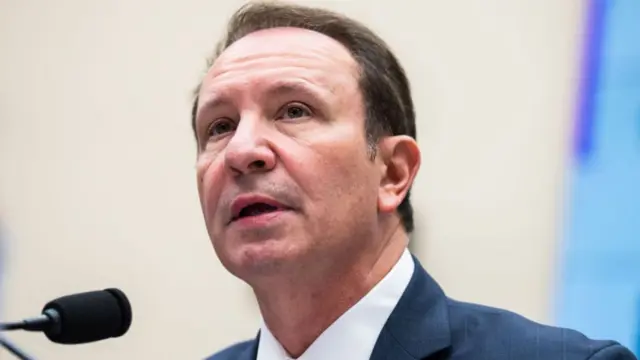 A close up of Landry, wearing a blue suit, speaking into a microphone