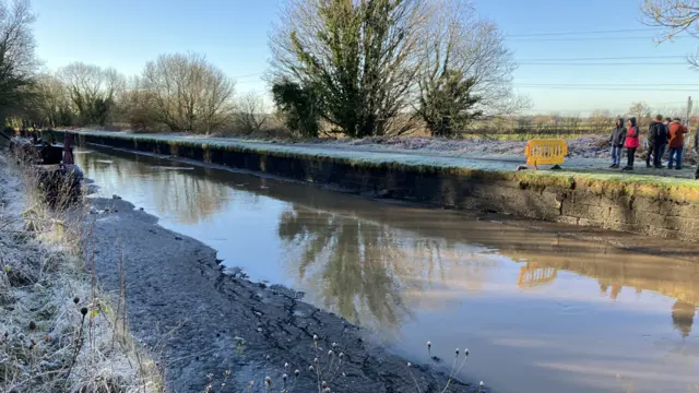 People stand next to Bridgewater Canal with a vastly-reduced water level due to a canal wall collapse