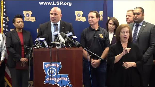 Christopher Raia, deputy assistant director of the FBI's counter-terrorism division, stands behind a podium with several microphones wearing a suit. He is standing next to several other people in front of a Louisiana State Police backdrop.