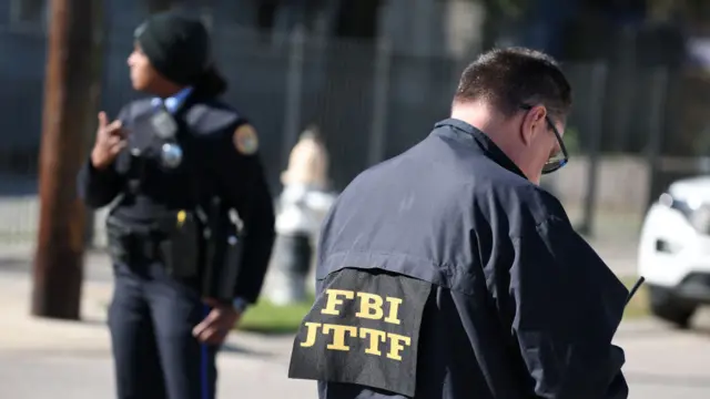 A picture of two people, one in a police officer's uniform and another with an FBI label on their back, stand on a street.