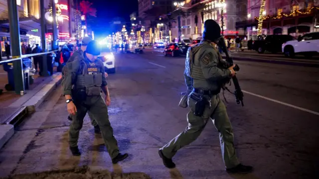 Police patrol the area near the scene where a vehicle drove into a crowd during New Year's celebrations. The two state officers are carrying assault rifles and the businesses on the street are alit with Christmas lights.