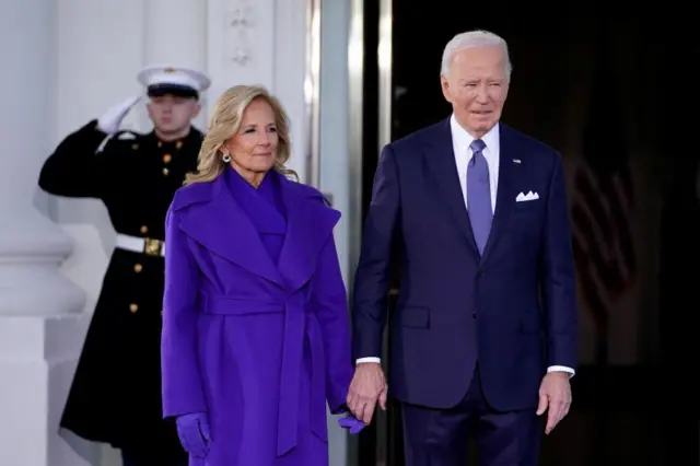 Jill Biden (left) and Joe Biden standing outside White House with a uniformed man saluting in the background